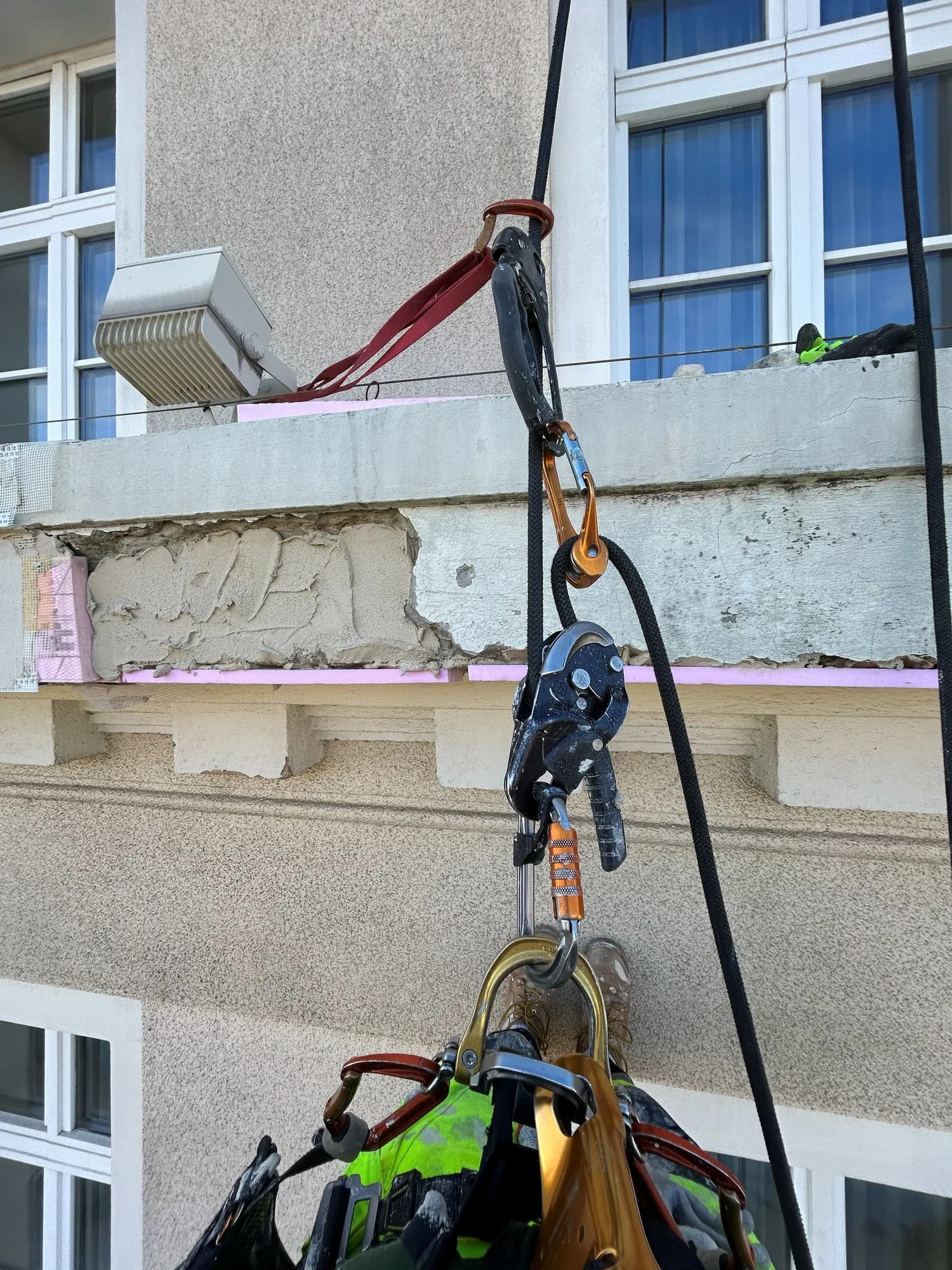Lanová technika zavesená pri poškodenej rímse bytového domu s obnaženou izoláciou