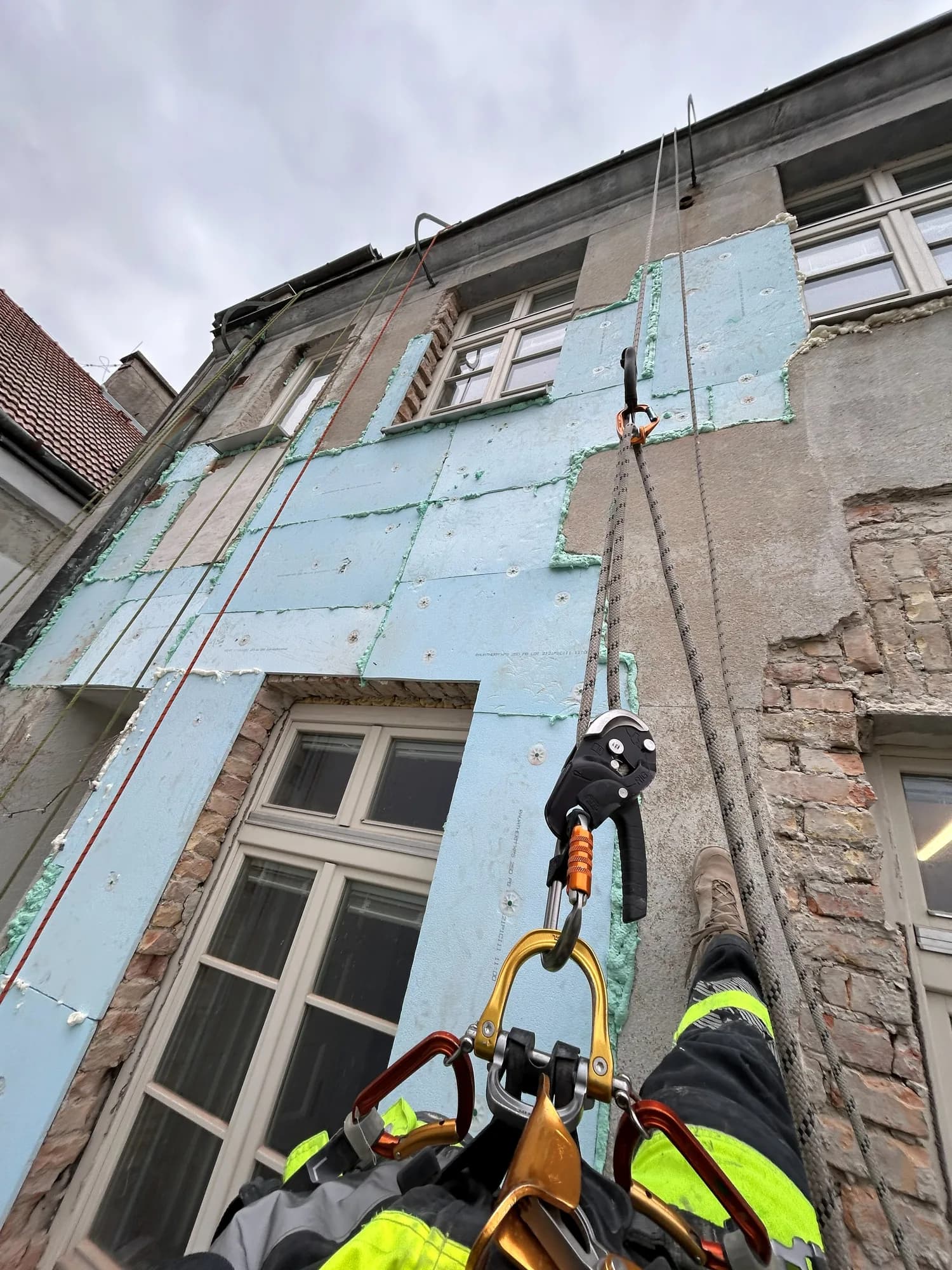 Oprava fasády staršej budovy z lanového prístupu, na stene osadené izolačné dosky