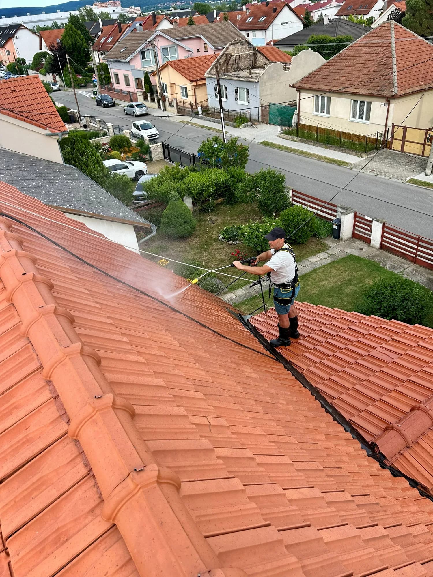 Pracovník čistí pálenú strešnú krytinu vysokotlakovým čističom, vzadu záhrada